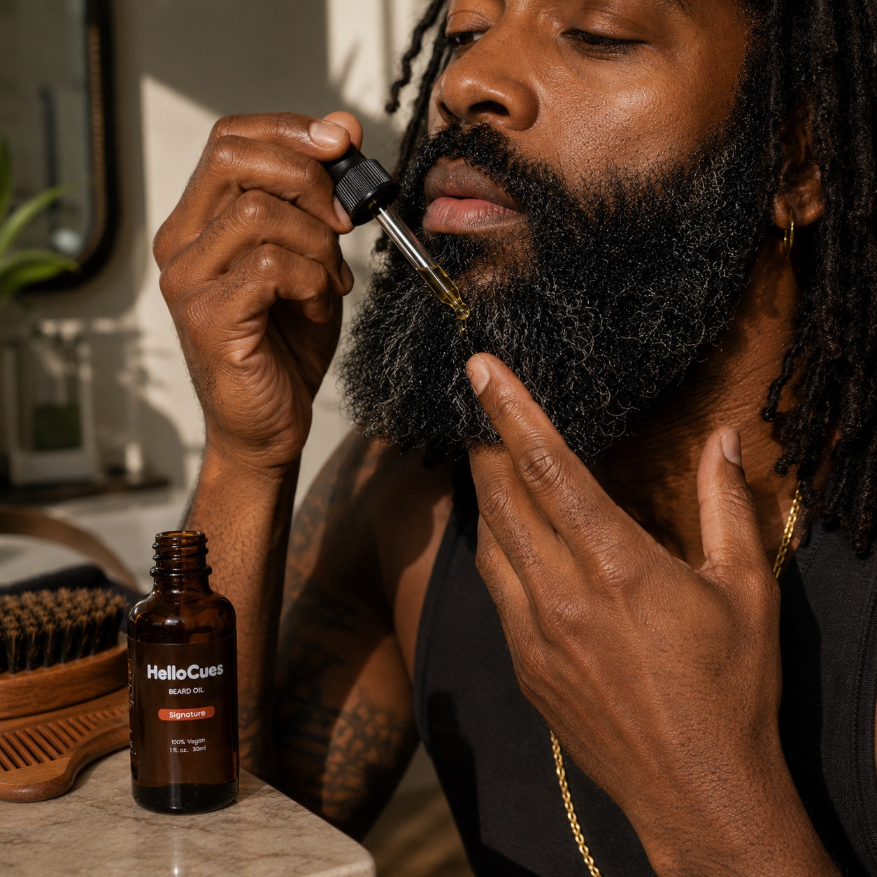 A man applying HelloCues Signature beard oil to his beard with the dropper, the oil bottle, a boar-bristle brush and a wooden comb on the counter beside him.