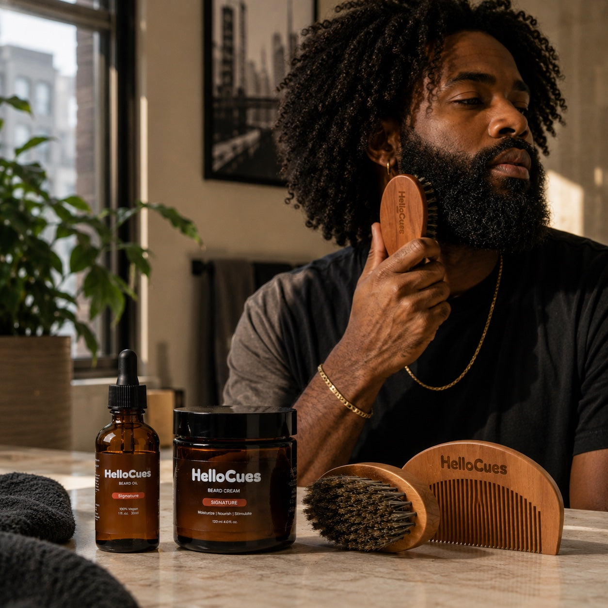 A man brushing his beard at a marble counter, with HelloCues Signature beard oil, a jar of Signature beard cream, a boar-bristle brush and a wooden HelloCues comb laid out in front of him.