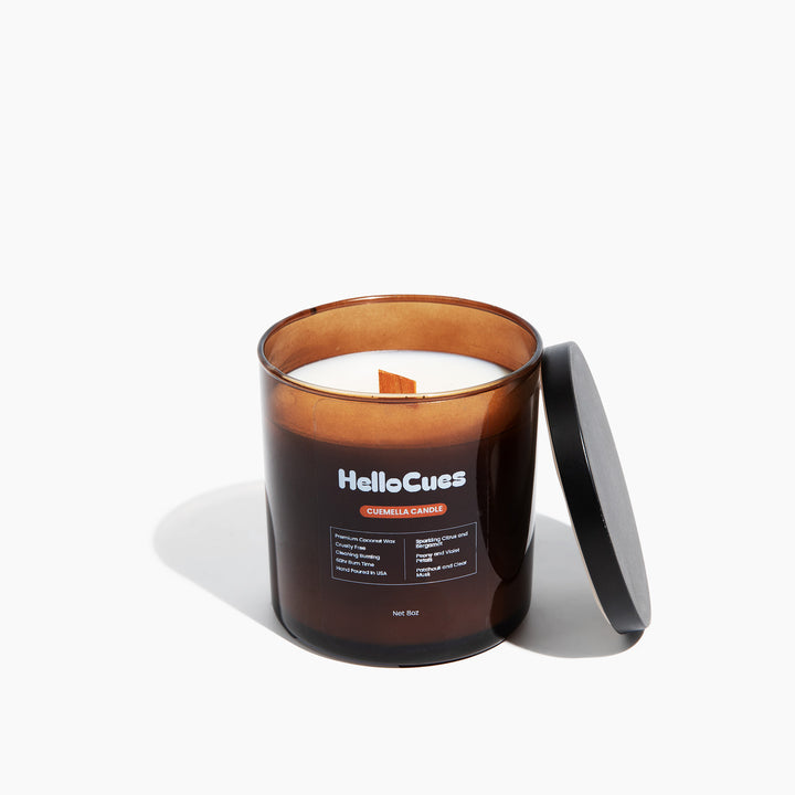 Cuemella scented candle in an amber glass jar with the black lid propped against it.
